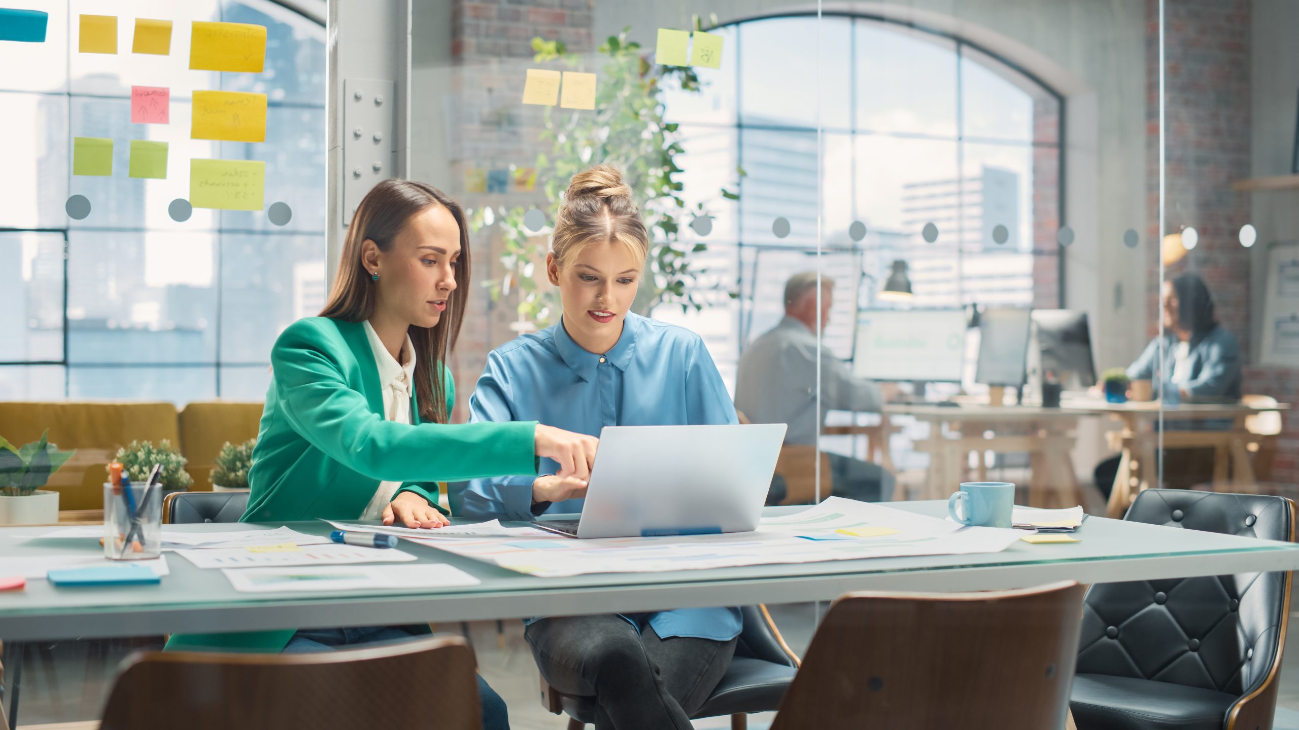 Portrait of Two Creative Colleagues Collaborating and Pointing at the Laptop in Modern Office. Female Manager Consults White Project Manager, They Brainstorm on the Project.